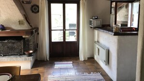 Une cuisine rustique avec un plafond en bois, une cheminée en pierre, une fenêtre avec des rideaux et un sol carrelé.
