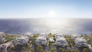 Uma área residencial costeira com edifícios de apartamentos modernos, vista clara para o mar e palmeiras.