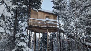 A wooden treehouse elevated on stilts amidst a snowy forest.