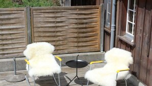 Two white furry chairs with yellow handles on a wooden deck, a small round table, and a wooden fence in the background.