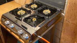 A kitchen with a gas stove, a wooden table, and a trash bin.