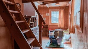 A wooden cabin interior with a staircase, a window, and a small table with a chair.