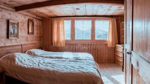 A wooden cabin bedroom with a bed, a window with curtains, and a dresser.