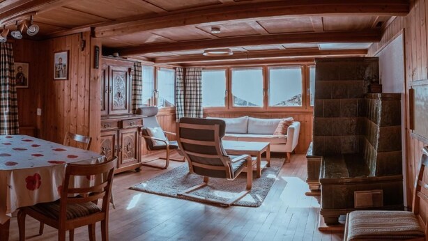 A cozy wooden cabin interior with a dining area, a sofa, and a fireplace.