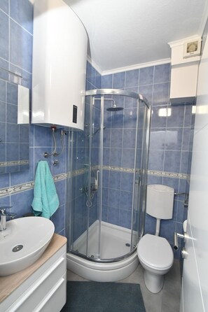 Une salle de bain avec une douche à parois de verre, des toilettes blanches et un lavabo doté d’un plan de travail en bois.