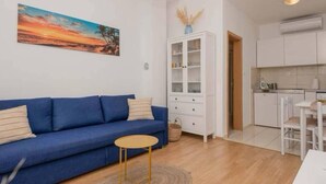 A living room with a blue sofa, a small round table, and a cabinet with glass doors. - Wohnung mit tollem Meerblick und 2 Bädern by Interhome (Podaca)