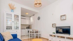 A modern living room with a blue sofa, a small round table, a TV on a white stand, and a kitchen area in the background. - Wohnung mit tollem Meerblick und 2 Bädern by Interhome (Podaca)