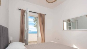 A bedroom with a bed, a window with curtains, a view of the sea, and a mirror on the wall. - Wohnung mit tollem Meerblick und 2 Bädern by Interhome (Podaca)