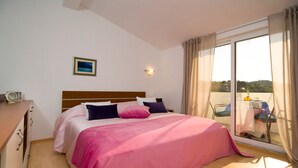 Un dormitorio con cama, mesita de noche, ventana con cortinas y vistas al exterior.