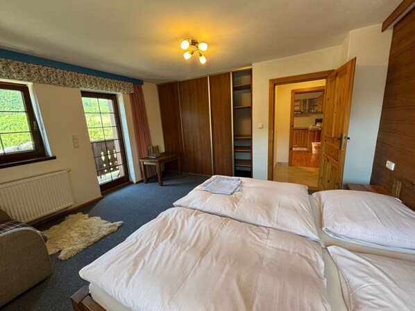 Une chambre avec deux lits, une armoire en bois, une petite table et une vue sur un jardin par la fenêtre.
