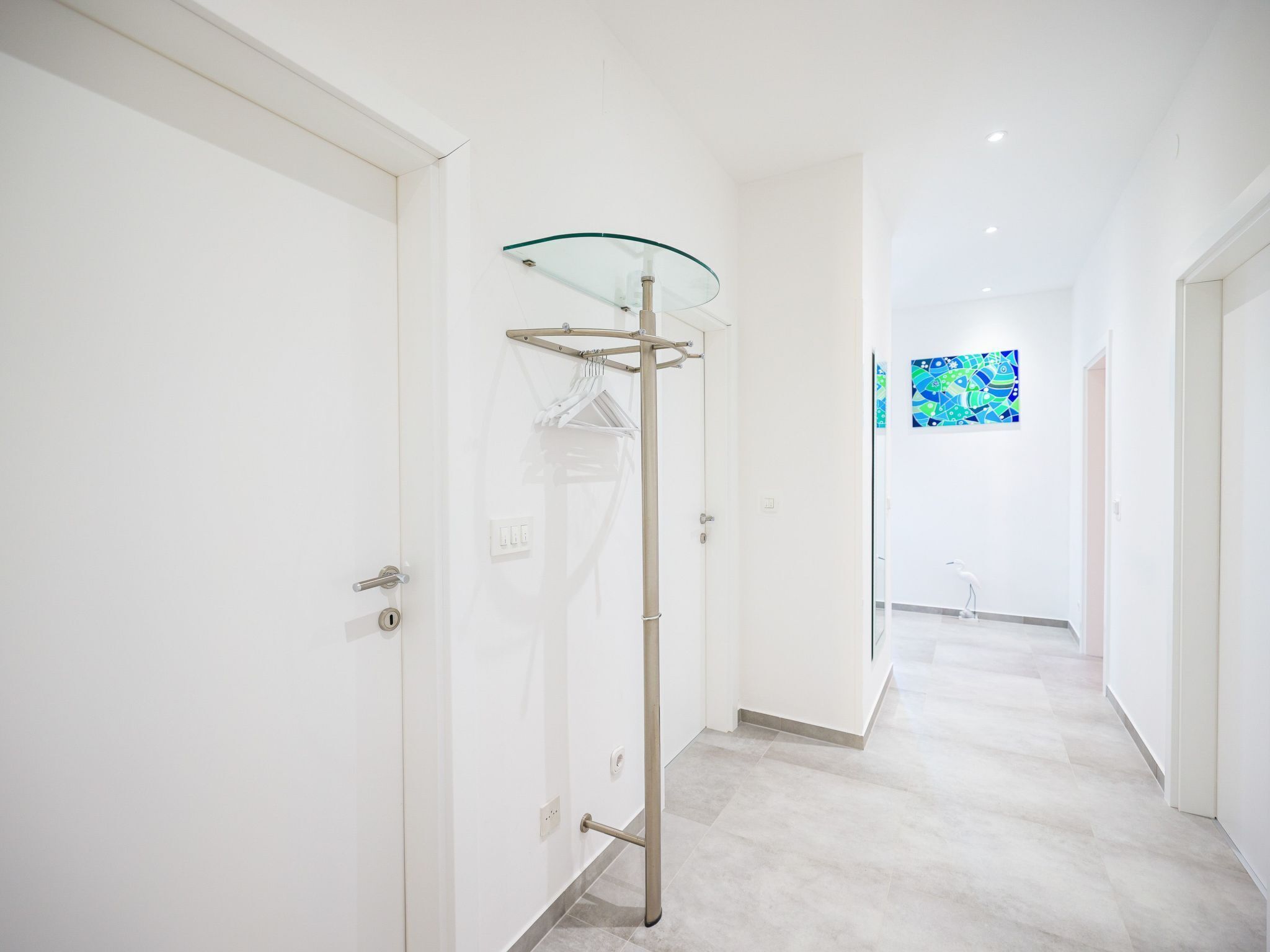 Un couloir moderne et minimaliste, doté d’une cabine de douche en verre, d’une porte avec une poignée et d’un porte-serviettes fixé au mur.