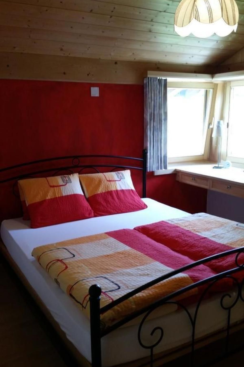 A bed with a metal frame, red and yellow bedding, and a window with curtains.