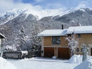 Une maison à deux étages, dont le toit est recouvert de neige, avec un garage et une vue sur les montagnes en arrière-plan.