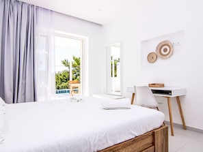 Ein modernes Schlafzimmer mit Bett, Schreibtisch und Blick auf Grün.