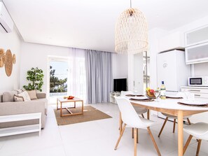 Ein modernes Wohnzimmer mit einer Couch, einem Esstisch, Stühlen, einem Fernseher und einer Küchenzeile mit einer Mikrowelle.
