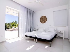 Ein modernes Hotelzimmer mit einem großen Bett, zwei Nachttischen, einem Deckenventilator und Blick auf Pool und Grünflächen.