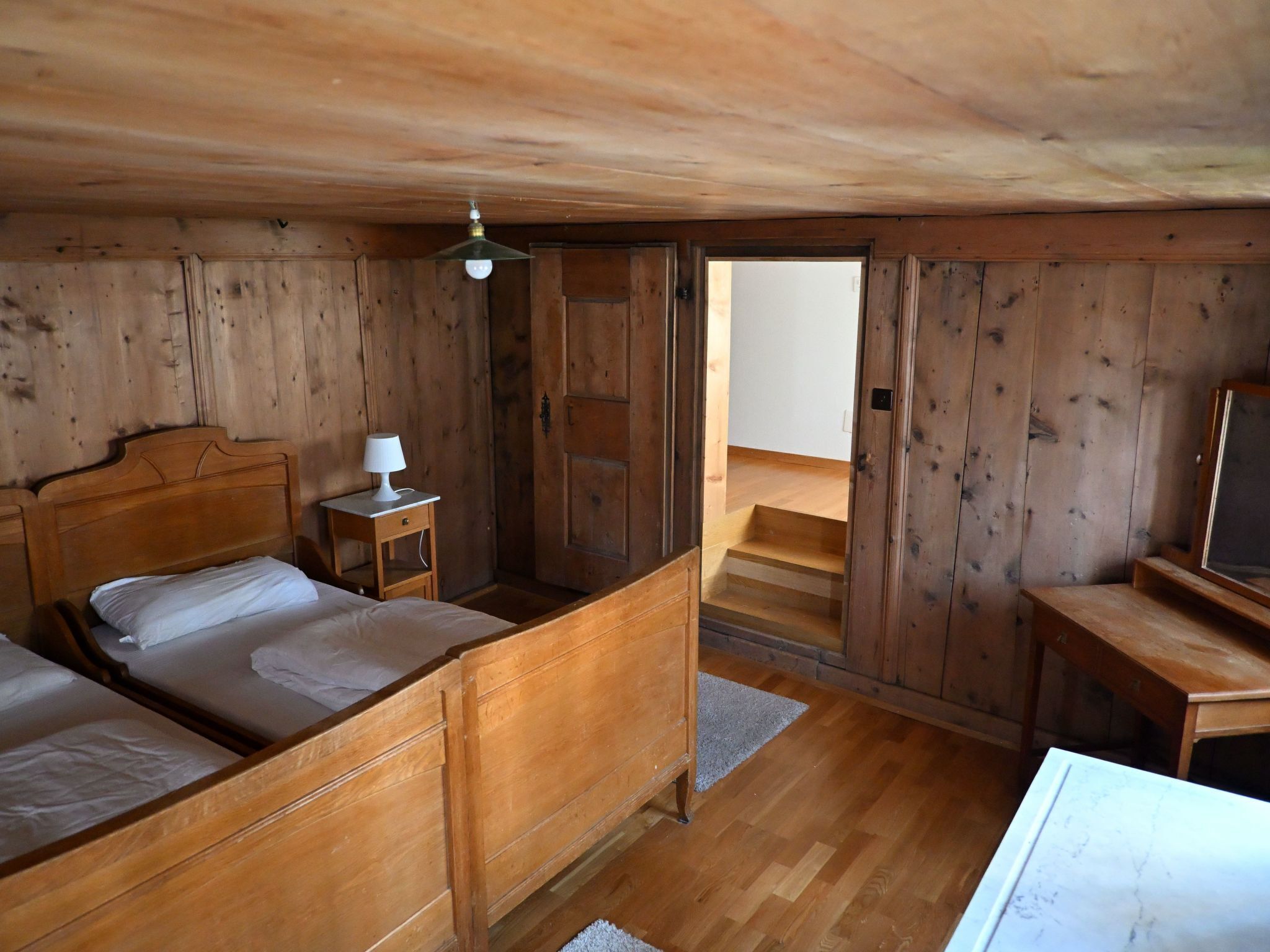 A wooden cabin bedroom with two beds, a nightstand, a desk, and a ceiling fan.