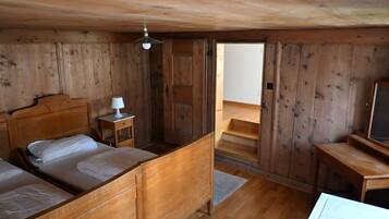 A wooden cabin bedroom with two beds, a nightstand, a desk, and a ceiling fan.