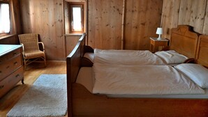 A wooden cabin bedroom with a bed, dresser, chair, and a small table with a lamp.