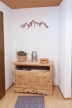 A wooden cabinet with a decorative wall decal of mountains, a woven basket, a metal container, and a bowl on top.