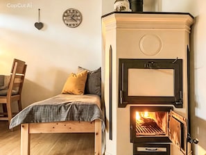 A cozy room with a bed, a wooden chair, a wall clock, and a wood-burning stove. - Kleinstein-Maass by Interhome (Samnaun)