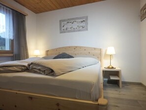 A neatly made bed with a headboard, two bedside lamps, a small bedside table, and a window with curtains.