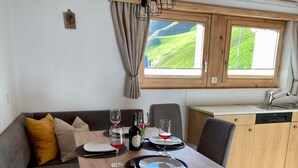 Eine kompakte Küche mit Essbereich, einem Holztisch für zwei Personen und Blick auf eine grüne Landschaft durch das Fenster.