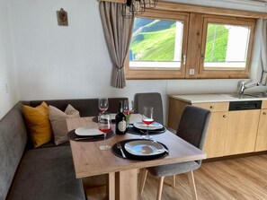 Ett kompakt kök med en matplats, ett träbord dukat för två personer och en utsikt över ett grönskande landskap genom fönstret.