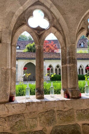 Ein steinerner Bogen mit freiem Blick auf einen Innenhof, einschließlich eines Gebäudes mit rotem Dach und einer Rose in einer Flasche.
