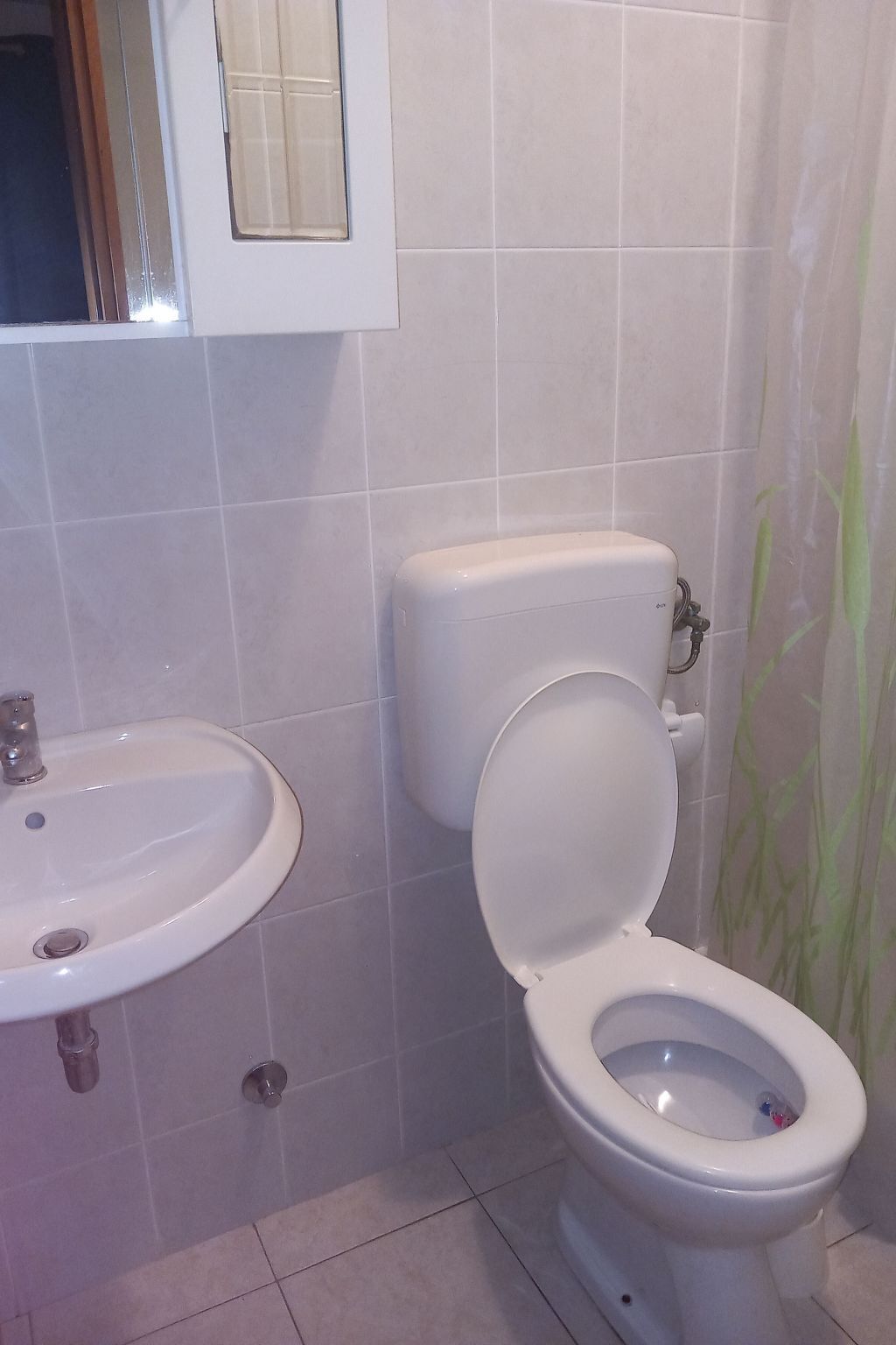 Une salle de bain avec un lavabo blanc, des toilettes et des murs carrelés.