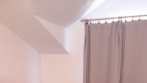 Ein ordentlich bezogenes Bett mit einer grauen Tagesdecke, Kissen und gerollten Handtüchern.