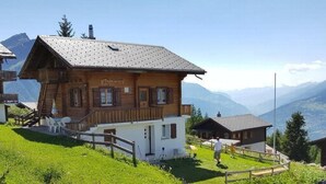 A wooden chalet with a balcony, surrounded by lush greenery and mountains in the background. - Adlerhorst by Interhome (Rosswald)