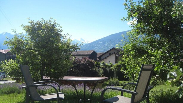 Un espace extérieur aménagé avec une table et deux chaises, entouré de verdure et offrant une vue sur la montagne.