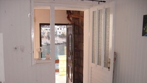 Een gang met een houten deur die leidt naar een balkon met uitzicht op een waterpartij en gebouwen.