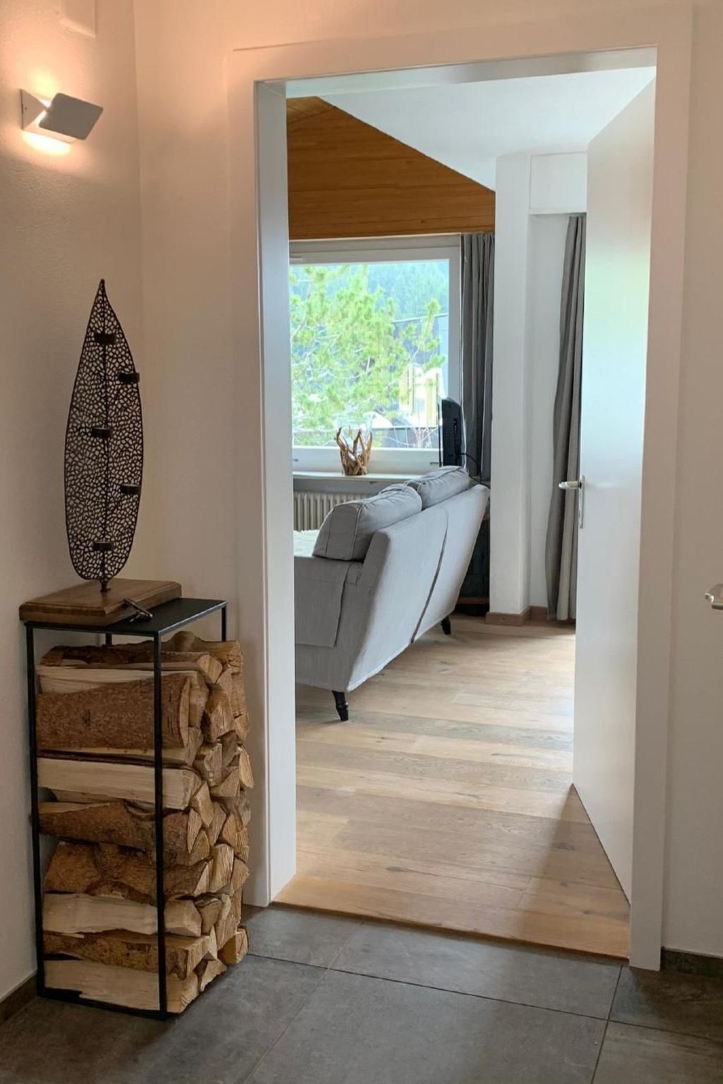 Un intérieur moderne avec un plafond en bois, un canapé gris et une pile de bois de chauffage.