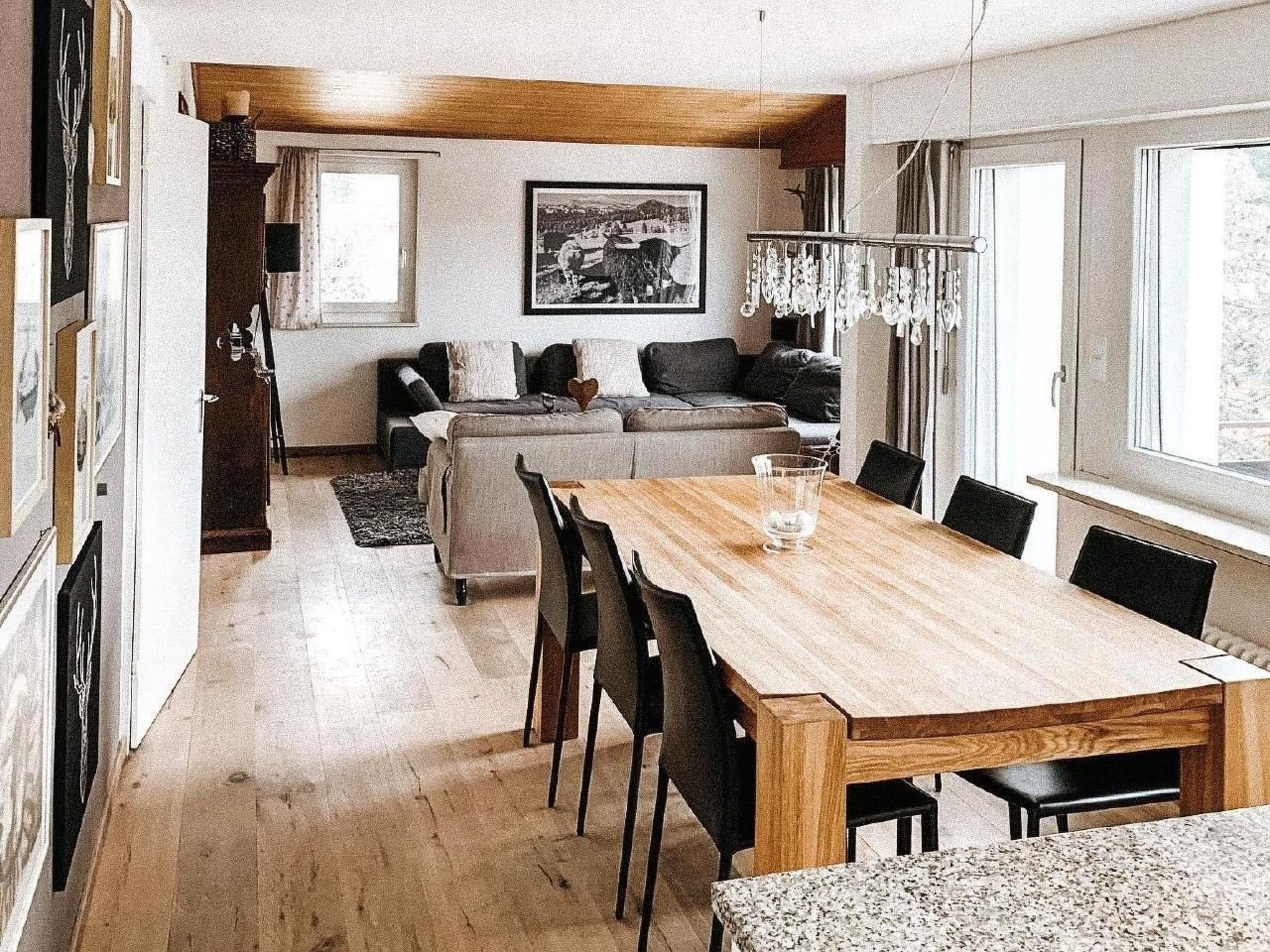 Un salon moderne avec une table à manger en bois, des chaises noires, un canapé et un lustre.