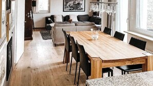 A modern living room with a wooden dining table, black chairs, a sofa, and a chandelier. - Haus Tschuetta - zentrale Lage in Valbella by Interhome (Valbella)