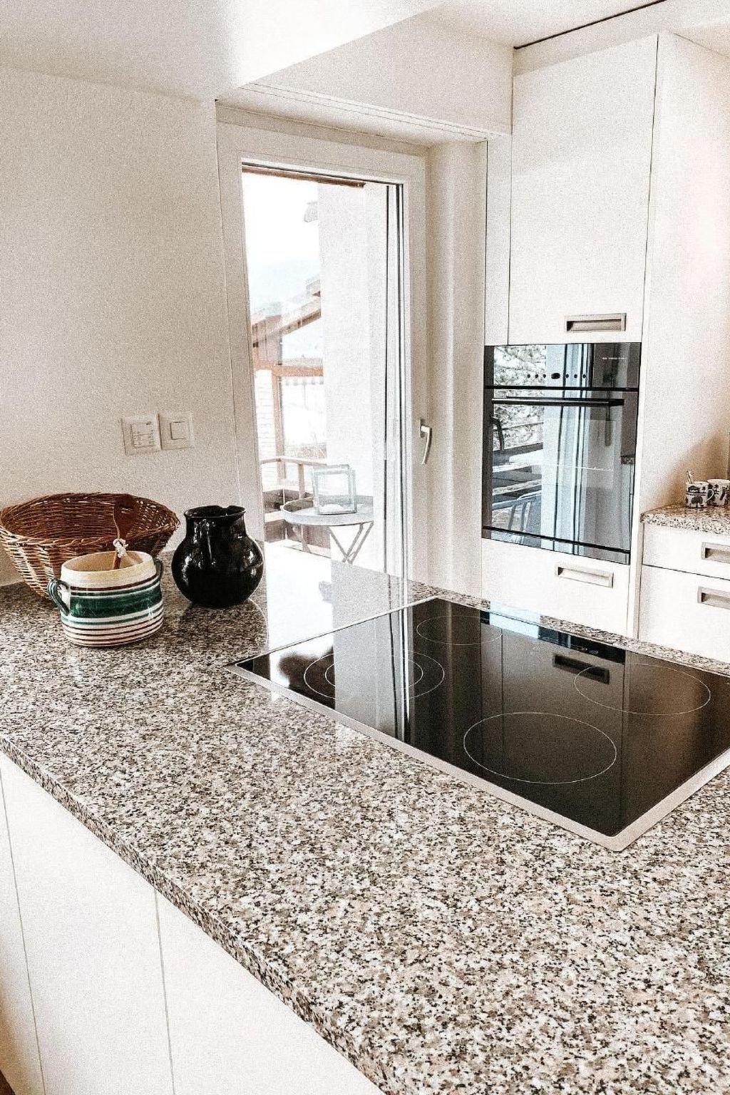 Une cuisine moderne dotée d’un plan de travail en granit, d’une plaque de cuisson à induction noire et d’appareils électroménagers en acier inoxydable.