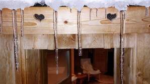 A wooden cabin with icicles hanging from the roof, a chair, and a cowhide rug inside.