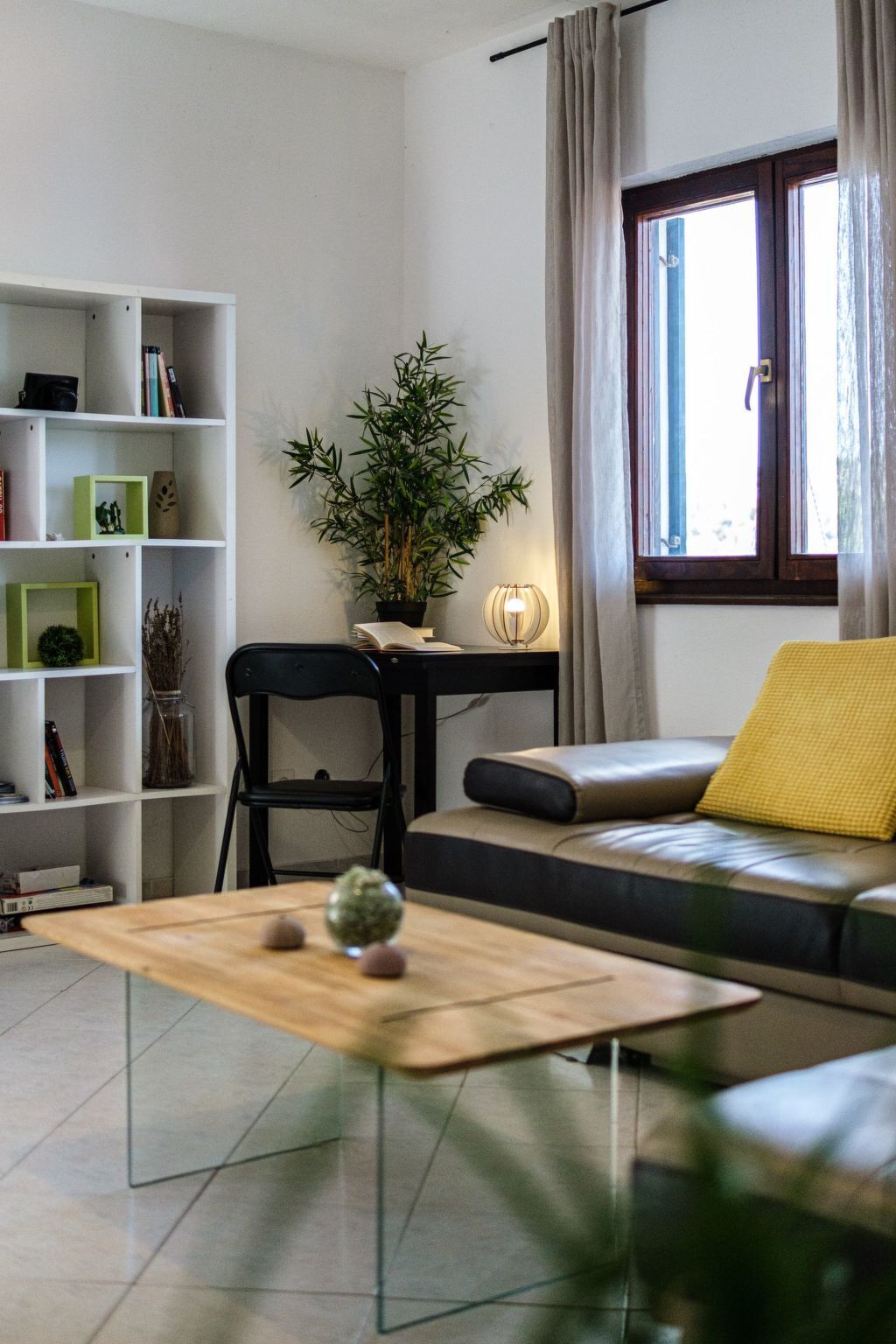 Una sala de estar moderna con un sofá, una mesa de centro, una estantería y una ventana con cortinas.