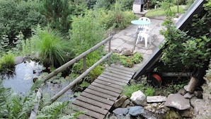 Een houten brug over een vijver met een terras en een barbecue.