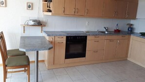Een compacte keuken met houten kastjes, een inbouwoven, een klein aanrecht en een stoel.