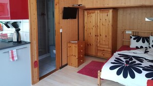 Ein Zimmer mit Holzwänden, einem Bett, einem Kleiderschrank, einem Fernseher und einer Küchenzeile.