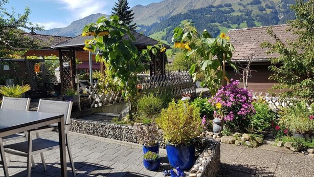 Eine Terrasse mit Tisch und Stühlen, umgeben von Topfpflanzen und Blick auf Berge.