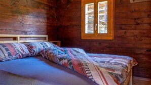 Un dormitorio acogedor de cabaña con cama de madera, ventana con vistas y techo de madera.