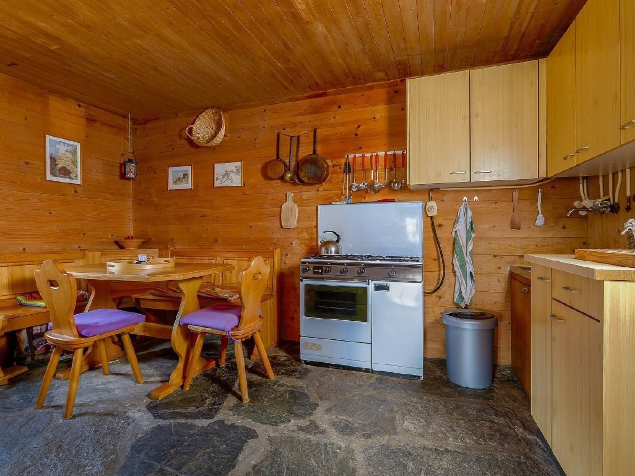 Une cuisine rustique avec des murs en bois, un sol en pierre, un poêle et des armoires en bois.
