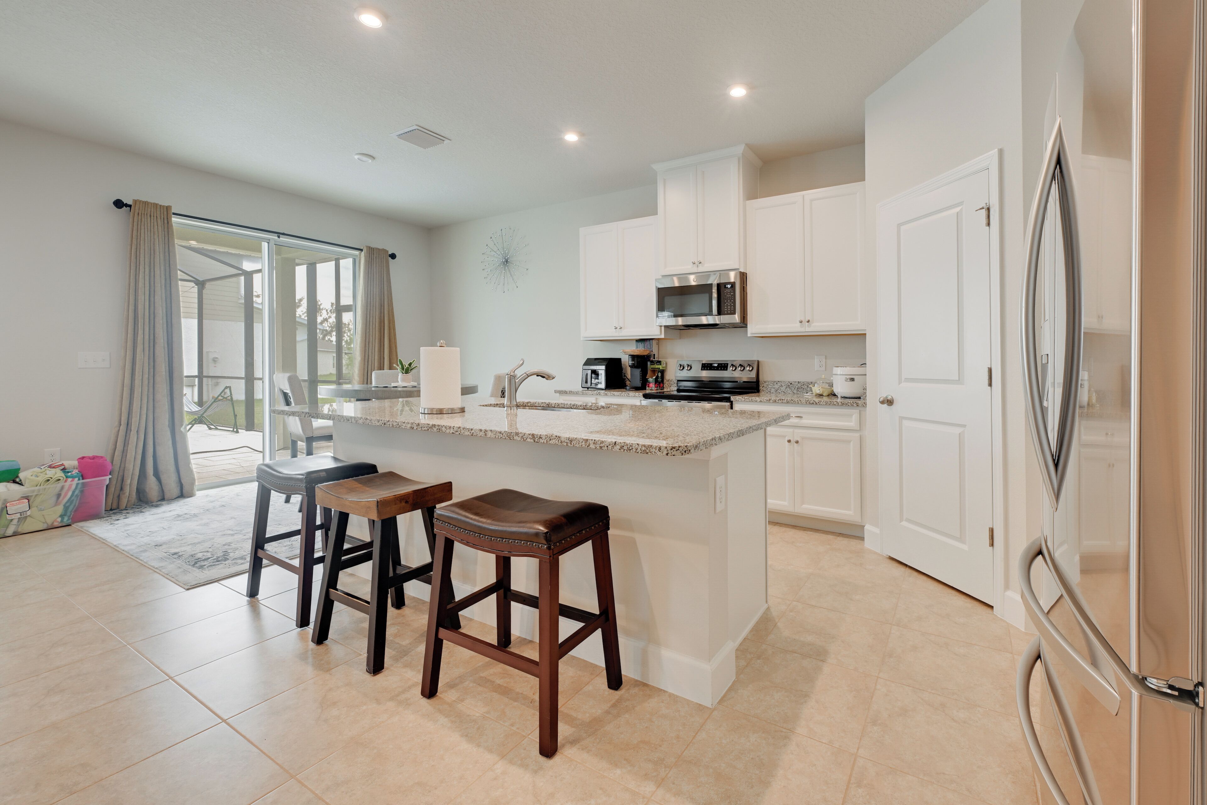 A modern kitchen with white cabinets, a granite countertop, and stainless steel appliances. There are two wooden stools at the island.