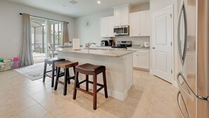 Una cocina moderna con armarios blancos, encimera de granito y electrodomésticos de acero inoxidable. Hay dos taburetes de madera en la isla.