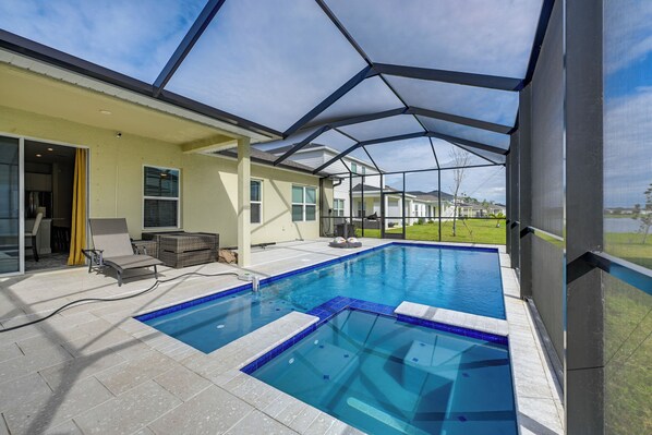 Una piscina con un recinto in vetro, una zona patio coperta e vista su un quartiere residenziale.