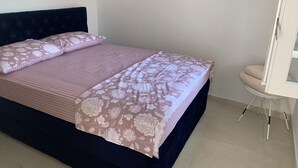 Un letto ben rifatto con copriletto e cuscini a motivi floreali, una testiera scura e una piccola sedia bianca con tavolino.
